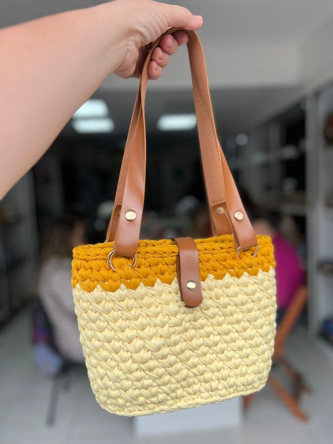 Bolsa de crochê em fio de malha amarela e creme, com alças de couro caramelo — segunda peça finalizada pela aluna